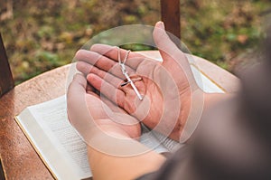 Woman holding a the cross in hand against the background of the bible.