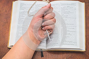 Woman holding a the cross in hand against the background of the bible.