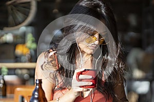 Woman holding a cup of coffee and listening to music with earphones at a coffee shop