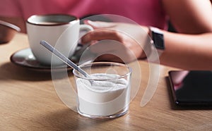 Woman holding a cup of coffee with milk and next to the sweetener