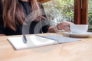 A woman holding a cup of coffee with notebook and pen on wooden table