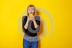 Woman holding cup of coffee on yellow color background