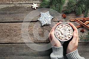 Woman holding cup of delicious hot chocolate with marshmallows at wooden table, top view. Space for text