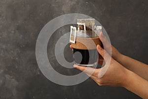 Woman holding cup with drip coffee bag on grey background, closeup. Space for text