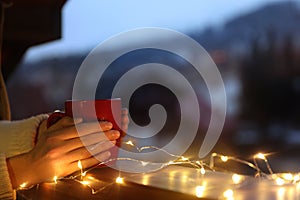 Woman holding cup of hot beverage on balcony decorated with Christmas lights, closeup with space for text