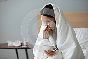 Woman holding cup with hot beverage and blows runny nose