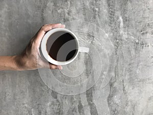 Woman holding a cup of hot black coffee with her left hand on cement board