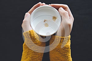 Woman holding cup of hot coffee on dark wooden table.