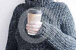 Woman holding cup of hot coffee on white wall, close up photo of hands in warm sweater with mug