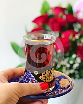 Woman holding cup of traditional Turkish tea, red roses background