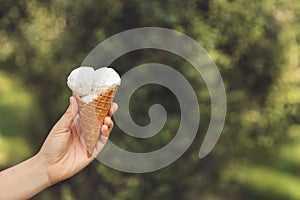 Woman holding delicious ice cream in waffle cone outdoors, closeup of hand. Space for text