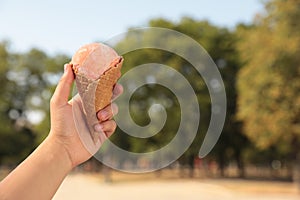 Woman holding delicious ice cream in waffle cone outdoors, closeup of hand. Space for text