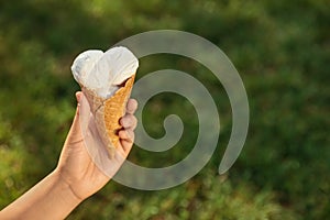 Woman holding delicious ice cream in waffle cone outdoors, closeup of hand. Space for text