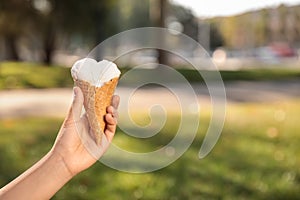 Woman holding delicious ice cream in waffle cone outdoors, closeup. Space for text