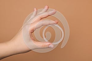 Woman holding diaphragm vaginal contraceptive ring on light brown background, closeup