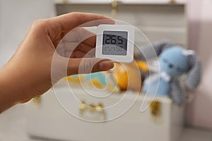 Woman holding digital hygrometer with thermometer on blurred background, closeup