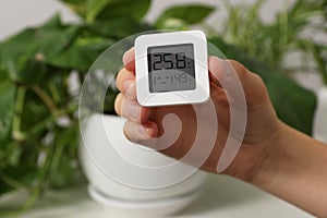 Woman holding digital hygrometer with thermometer on blurred background, closeup