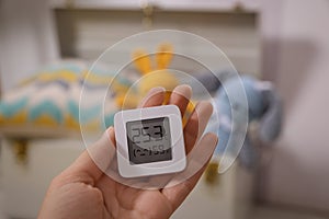 Woman holding digital hygrometer with thermometer on blurred background, closeup