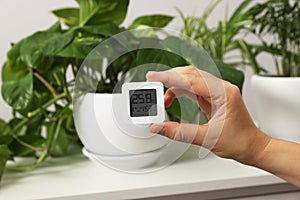 Woman holding digital hygrometer with thermometer near plants indoors, closeup