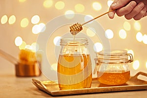 Woman holding dipper over jar with honey on table