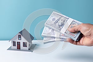 Woman holding dollar bill in hand with white house model background. Mortgage loan approval home loan and insurance concept