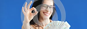 Woman holding dollar bills in her hands and showing ok gesture closeup