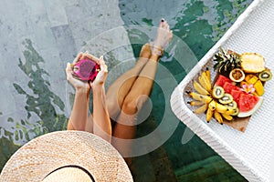 Woman holding dragon fruit near tray with served Breakfast in swimming pool.
