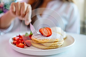 A woman holding and eating pancakes with strawberries and whipped cream