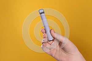 Woman holding electronic cigarette on orange background, closeup