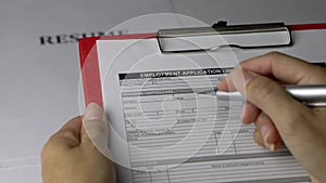 Woman holding an employment application form on top of resume on office table.