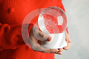 Woman holding empty snow globe on light background