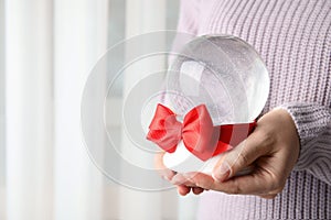 Woman holding empty snow globe with red bow, closeup. Space for text