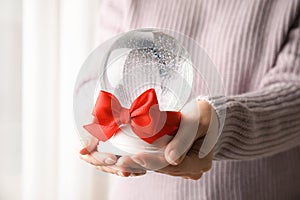 Woman holding empty snow globe with red bow indoors, closeup.