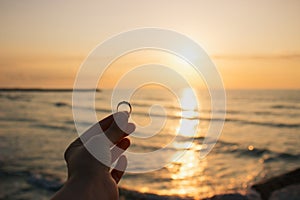 Woman holding the engagement ring in hand in the time sunrise on sea. An offer of marriage on beach of Italy