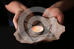 Woman holding fabric with star of David and burning candle on black background, closeup. Holocaust memory day