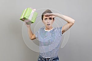 Woman holding far away with open mouth and hand over forehead, holding present box.