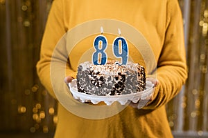 Woman holding a festive cake with number 89 candles while celebrating birthday party. Birthday holiday party people