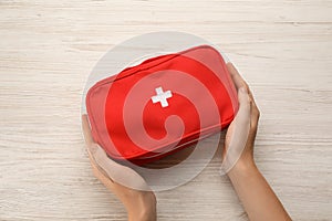 Woman holding first aid kit bag at white wooden table, top view