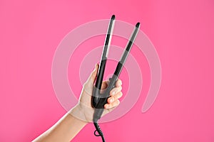 Woman holding flat hair iron on pink background, closeup