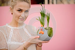 Woman holding a flower pot in the shape of grey chicken with the narcissus with green leaves