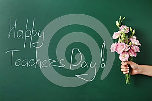 Woman holding flowers near green chalkboard with inscription HAPPY TEACHER`S DAY