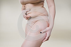 Woman holding fold of skin, cellulite on female body, beige background