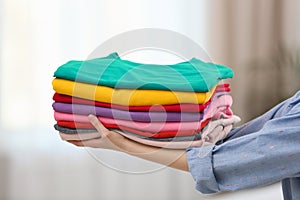 Woman holding folded clean clothes indoors. Laundry day