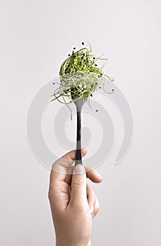 Woman holding fork with microgreen over white background