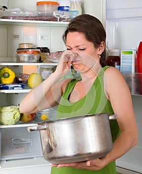 Woman holding foul food near fridge