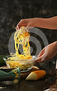 Woman holding fresh zucchini spaghetti over bowl