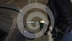 Woman holding fuel nozzle and refuel car in gas station at night. Side view