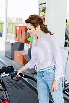 Woman holding fuel pump while refueling automobile with benzine at gas station