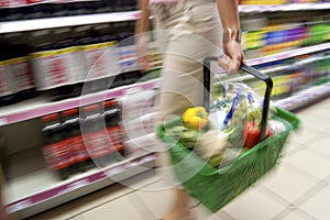 Woman Holding Full Shopping Basket Along Soda Aisle in Supermarket