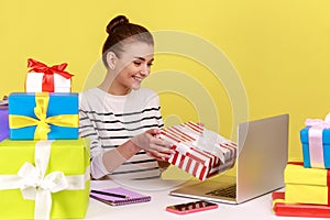 Woman holding gift box and looking at laptop screen, giving birthday present, online celebration.